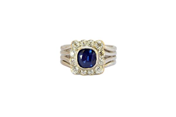 A sapphire and diamond set cluster ring, mounted with the cushion shaped sapphire at the centre, in a surround of twelve cushion shaped diamonds, the