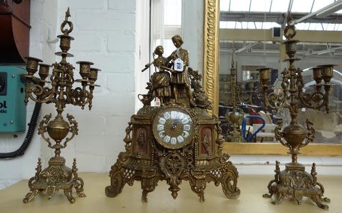 An early 20th century brass and marble mounted clock garniture, the clock decorated with a 17th century courting couple, 45cm high. (3)