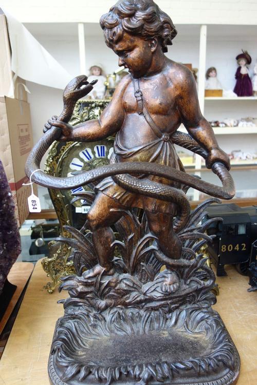 A Coalbrookdale cast iron stick stand, mid-19th century, modelled and cast with the infant Hercules wrestling a snake, with foliate cast drip pan (a.f