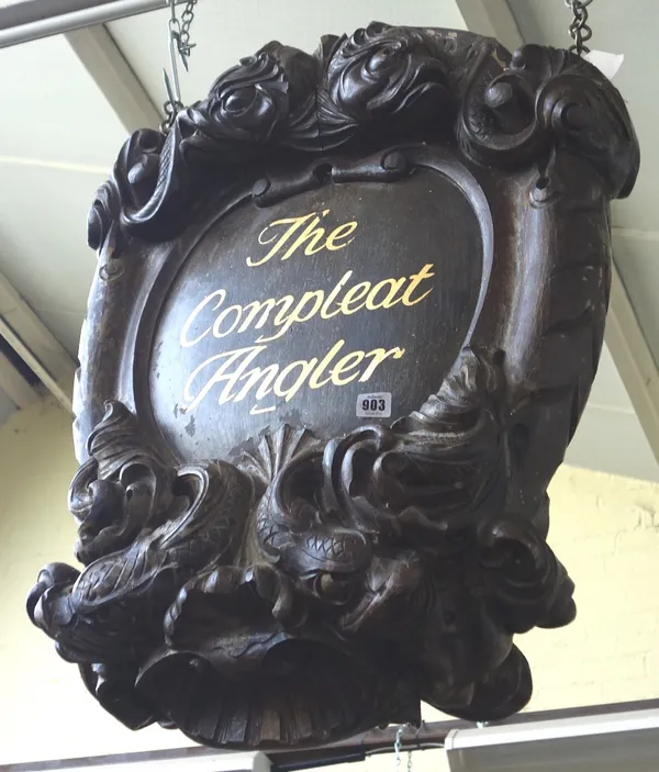 A faux oak shop sign 'The Complete Angler', carved with mythological dolphins and shell detail with gilt lettering to the centre and iron hanging ring
