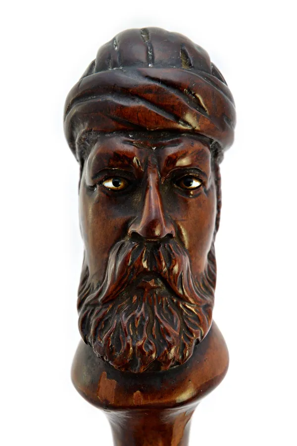A black thorn walking stick, 19th century, the pommel finely carved with the head of an Arab man, with inset hardstone eyes, 82cm long.  Illustrated