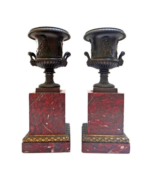 A pair of French Restauration bronze and parcel gilt urns, circa 1825, each cast with putti in relief, emblematic of the seasons, on square marble pli