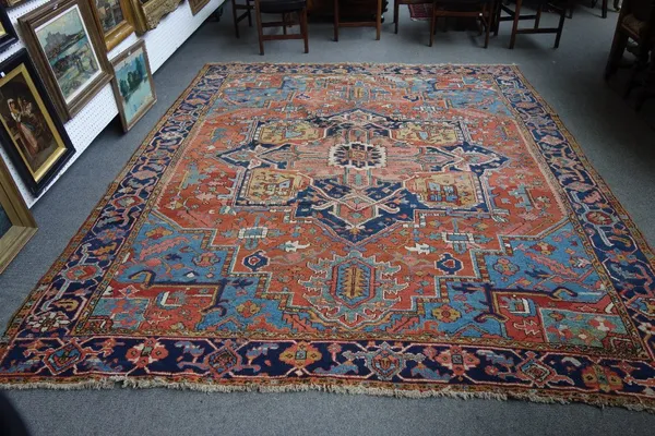 A Heriz carpet, Persian, the madder field with a bold medallion, matching spandrels, an indigo palmette and vine border, 326cm x 262cm.