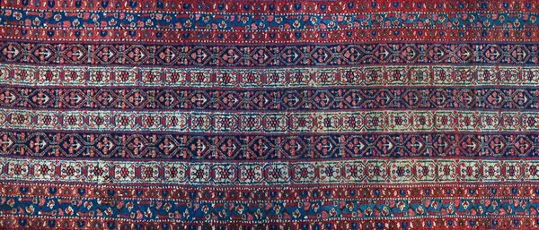 A West Persian runner, the field with six bands of connecting flower and bracket design, an indigo flower and ribbon border, 576cm x 106cm.  Illustrat