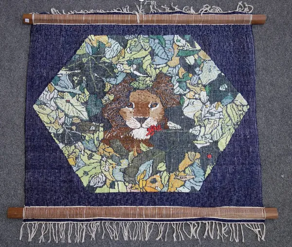 A needlework tapestry worked by Fleur Cowles, depicting a lion's head in a hexagonal flower filled panel, blue border, signed, 78cm x 100cm; and anoth