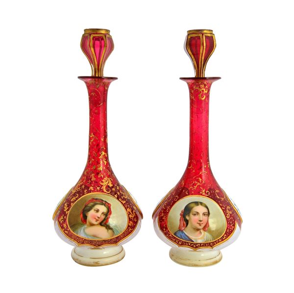 A pair of Bohemian cranberry glass and enamel overlay decanters and stoppers, 19th century, the enamel decorated with opposing female portraits and fo