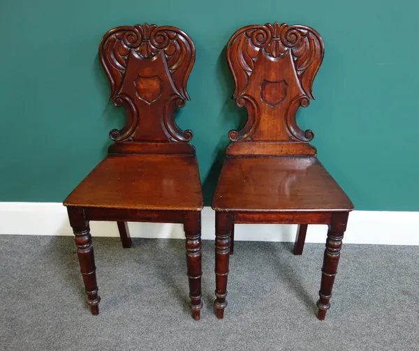 A pair of Victorian mahogany hall chairs, with shield centred carved scroll back, on turned supports (2).