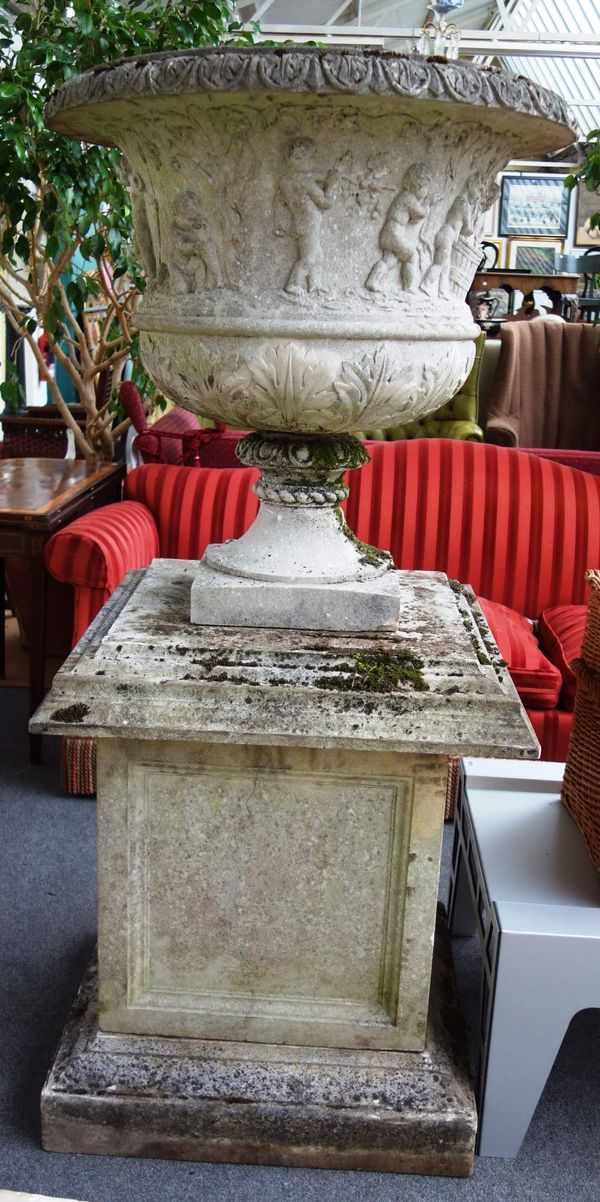 A large composite stone urn, the body relief moulded with cherubs, on turned socle and stepped square pedestal, 160cm high.