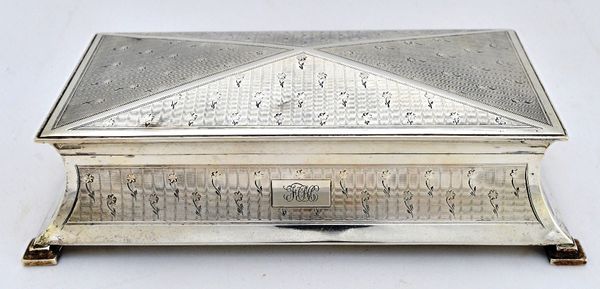 A silver shaped rectangular table cigarette box, of waisted form with a domed lid, the exterior engraved with floral sprays, on an engine turned groun