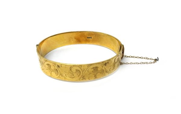 A 9ct gold oval hinged bangle, the front with feathered scroll engraved decoration, on a snap clasp, fitted with a safety chain, weight 26.6 gms, Birm