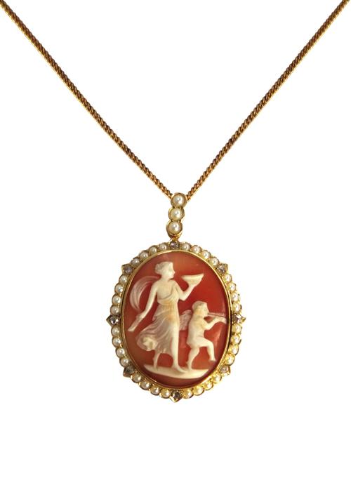 A gold, seed pearl and rose diamond set oval shell cameo pendant, the cameo carved as a classical female figure holding a cup and with a cherub blowin