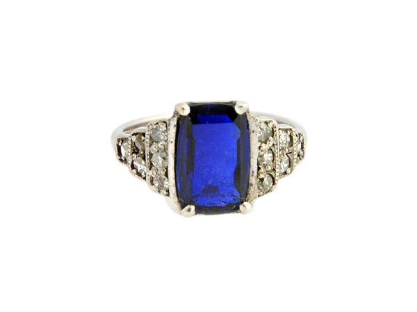 A white gold, sapphire and diamond ring, claw set with the curved rectangular cut sapphire to the centre, between diamond set stepped shoulders, in a