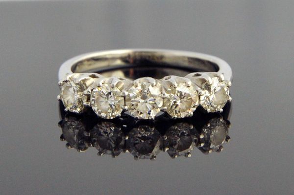 A platinum and diamond five stone ring, claw set with a row of circular cut diamonds, ring size O, with a case.  Illustrated