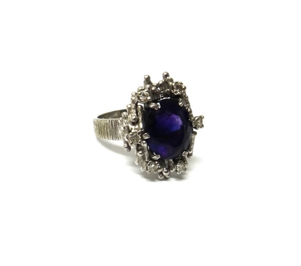 An 18ct white gold, amethyst and diamond ring, claw set with the oval cut amethyst at the centre, in a surround of six circular cut diamonds, the moun