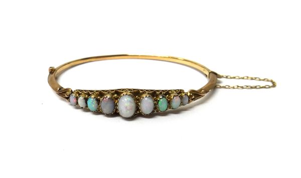 A 9ct gold and opal set oval hinged bangle, mounted with a row of nine oval opals graduating in size to the centre stone, the mount decorated with scr