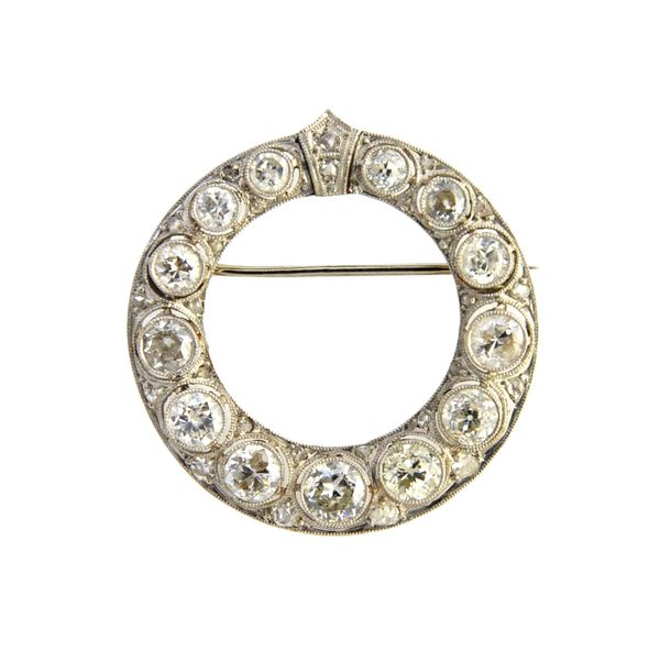 A diamond brooch, in a circular openwork design, mounted with a row of graduated circular cut diamonds in mille-grain settings and further mounted wit