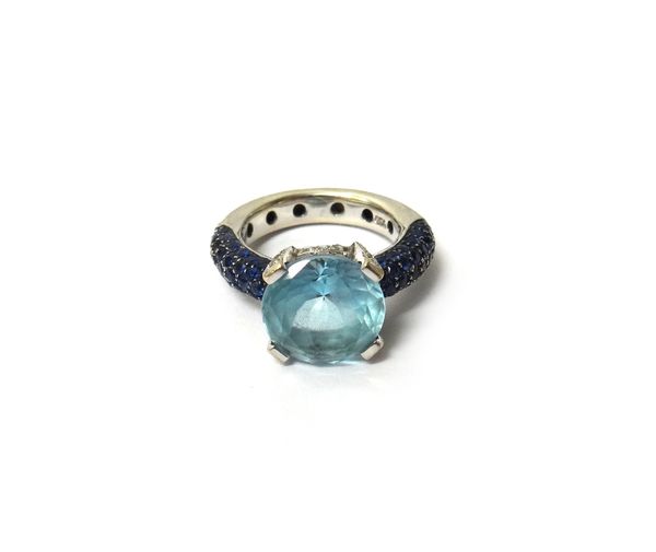 A white gold ring, claw set with a circular cut pale blue topaz to the centre, between sapphire set shoulders, the claws and the sides of the ring mou