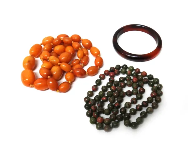 A single row necklace of graduated oval vary coloured butterscotch coloured amber beads, a stone bead necklace and a costume bangle, gross weight of a