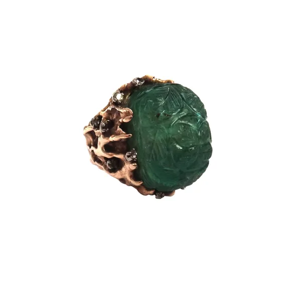 A gold, carved emerald and diamond ring, the carved emerald having foliate decoration, possibly Indian, the mount in a cast abstract design, mounted w