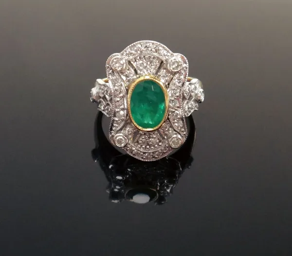 An 18ct gold, emerald and diamond cluster ring, in a curved panel shaped design, collet set with the oval cut emerald at the centre and otherwise moun