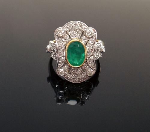 An 18ct gold, emerald and diamond cluster ring, in a curved panel shaped design, collet set with the oval cut emerald at the centre and otherwise moun