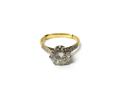 A gold and diamond set single stone ring, claw set with the principal circular cut diamond at the centre, between diamond three stone shoulders, the p