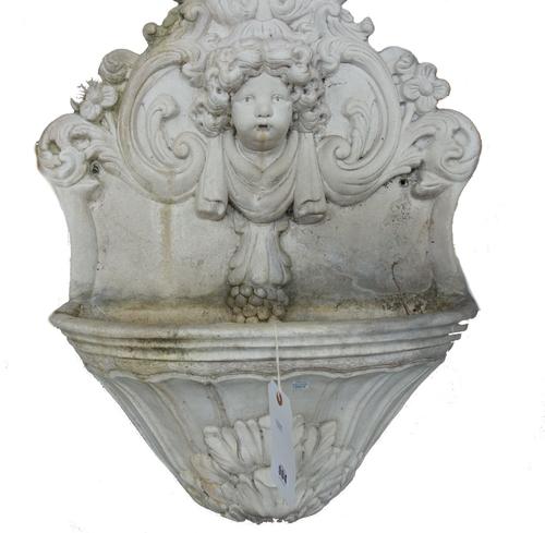 A reconstituted white marble water stoop with relief carved cherub mask and foliate scrolls over a half block carved bowl, 70cm high. Property from th
