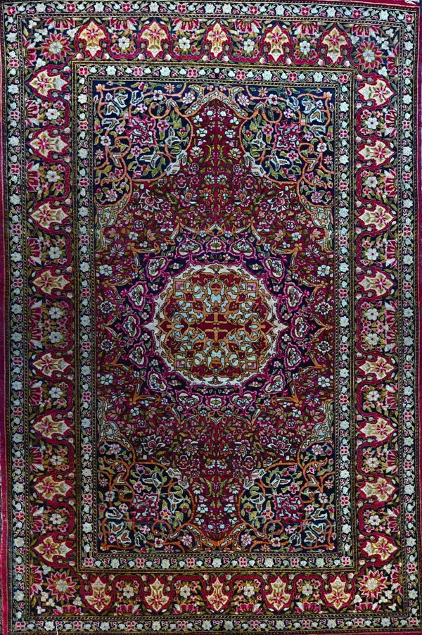 A Kerman rug, Persian, the madder field with an ivory and black roundel, matching spandrels, all with floral sprays, a complementary border, 212cm x 1