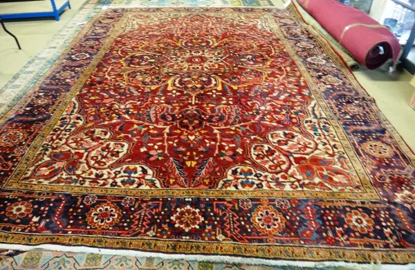 An Heriz carpet, Persian, the dark madder field with a bold central rosette medallion, ivory spandrels, all with floral vines, with an indigo rosette,