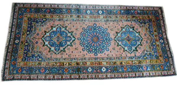 A Moroccan carpet, the pink field with three bold medallions, minor spandrels, a wide indigo palmette and floral spray border, 665cm x 314cm.