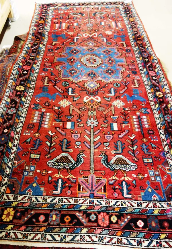 A West Persian rug, the madder field with a bold indigo medallion, pairs of peacocks, flags, animals, birds, flowers and plants, a black flower and tr