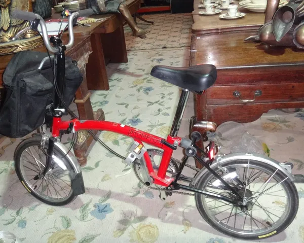 A red painted Brompton folding bike with matching pannier 'D' lock helmet and pump.