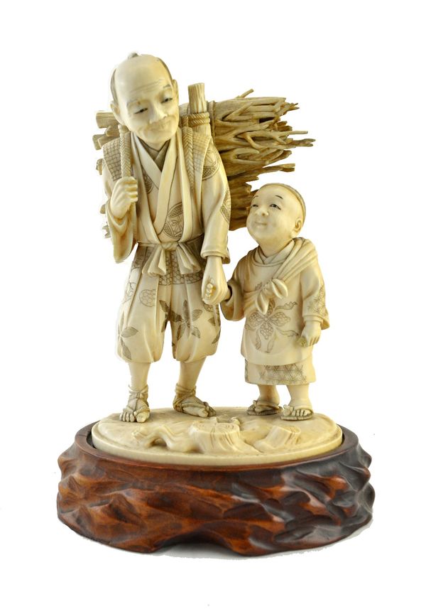 A Japanese ivory okimono of a man and child, Meiji period, standing holding hands, the elderly man carrying bundles of sticks across his back, (a.f),