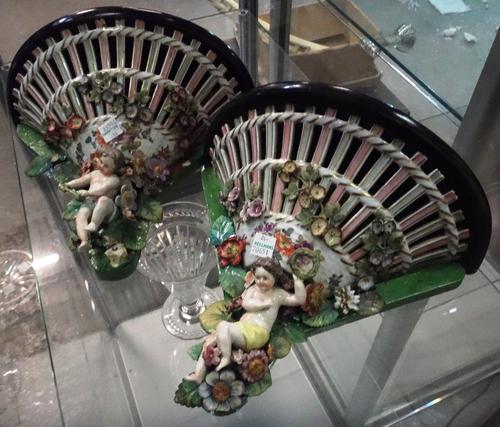A pair of ceramic wall shelves, moulded with flowers and putti.