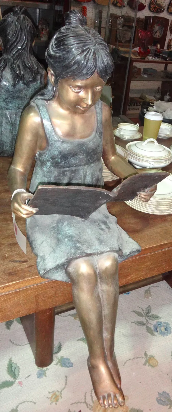 A 20th century bronze seated figure of a girl reading.