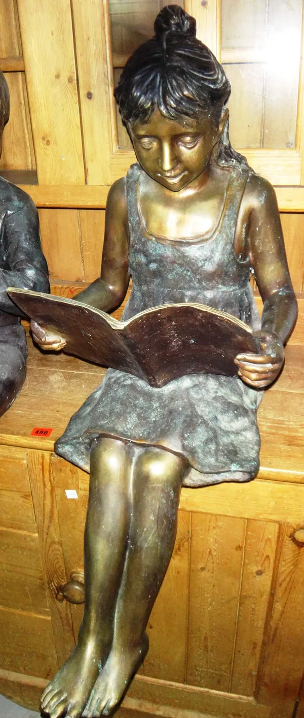 A 20th century bronze figure of a seated girl reading.