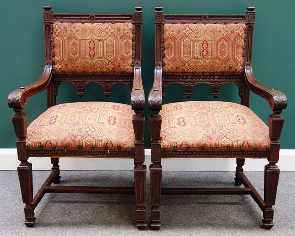 A pair of Victorian carved oak square back open armchairs on tapering square supports.