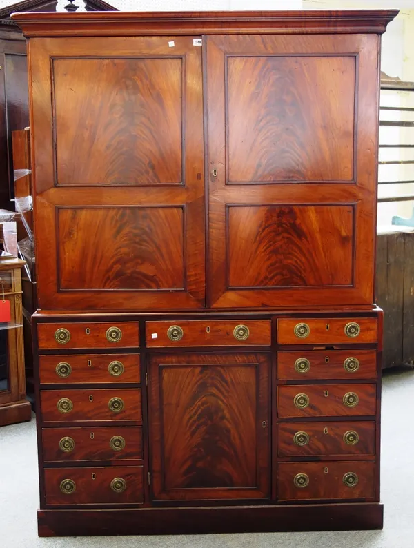 A 19th century mahogany estate cupboard the pair of panel doors enclosing four pull out trays, the base with an arrangement of eleven drawers around t