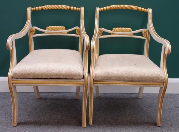 A pair of Regency style cream painted parcel gilt open armchairs on sabre supports.