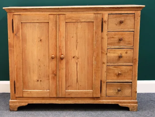 A 19th century pine side cabinet, with pair of panel doors enclosing shelves, mounted with five short drawers to the right hand side, on bracket feet,