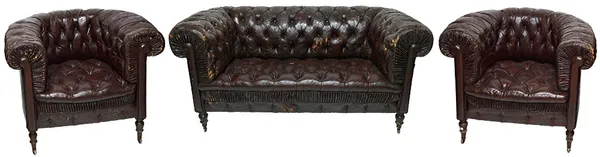 An early 20th century button back rouge leather upholstered Chesterfield three piece suite, to comprise a sofa and a pair of tub chairs, on turned sta