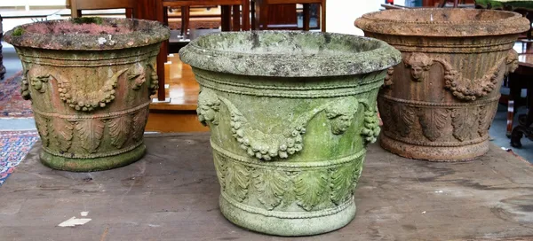 A set of three reconstituted stone tapering circular planters relief moulded with female masks and fruiting vines, 60cm wide x 57cm high.