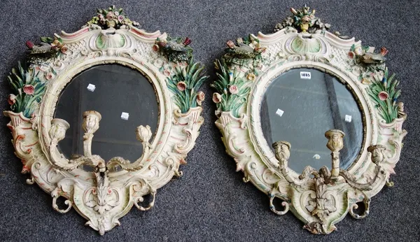 A pair of 19th century Continental polychrome painted wall mirrors, extensively moulded with shells, songbirds and flowering cornucopia about the oval