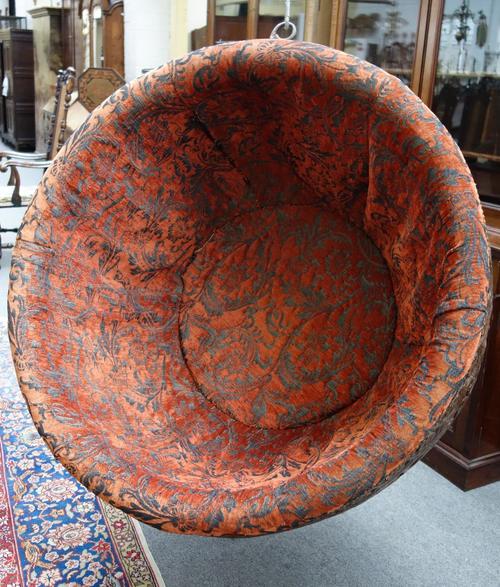A hanging chair, the cushion upholstered interior within an extensively carved shell back frame of stylized flowers in interlaced arcades, 125cm high.