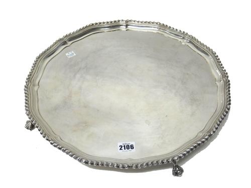 A silver salver, of shaped circular form, decorated with a gadrooned rim and raised on four ball and claw feet, in the late 18th century taste, London