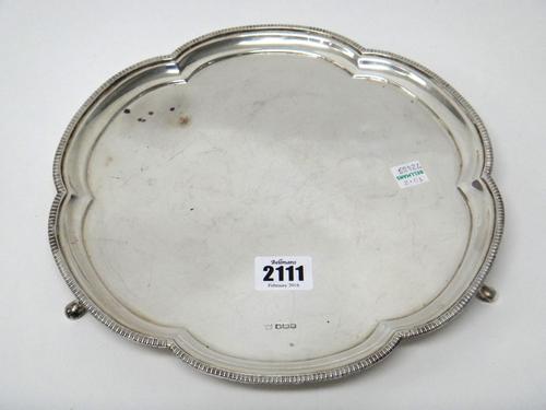 A silver salver, of curved hexagonal form, having a decorated border and raised on three feet, diameter 26cm, weight 592 gms, Sheffield 1930.