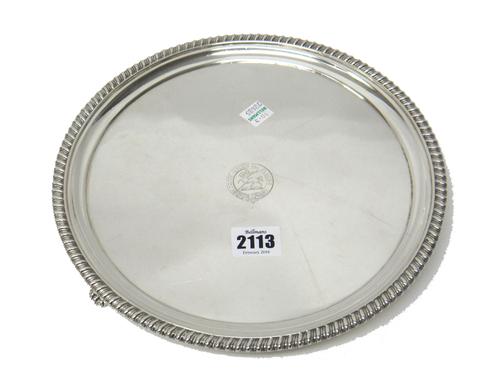 A George III silver circular salver, engraved with a crest and a motto to the centre and having a gadrooned rim, raised on three feet, diameter 25.5cm