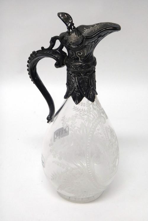 A Victorian silver mounted glass claret jug, the body etched with three putto within a beaded oval surround, decorated with fern sprays and lily of th