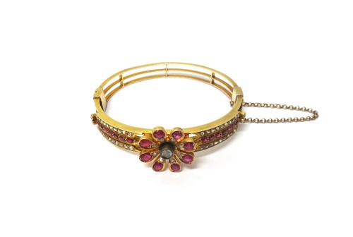 A gold, ruby and diamond set oval hinged bangle, the front with a flowerhead motif, the sides mounted with rows of rose diamonds and cushion shaped ru