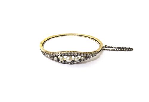 A diamond and cultured pearl set oval hinged bangle, the front mounted with a row of five graduated cultured pearls, in a pierced openwork surround, m